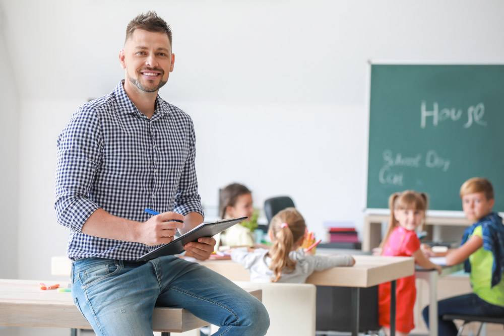 Male teacher smiling with kids in the background. Education background check concept.