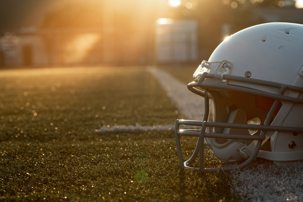Football helmet on turf at sunset.
