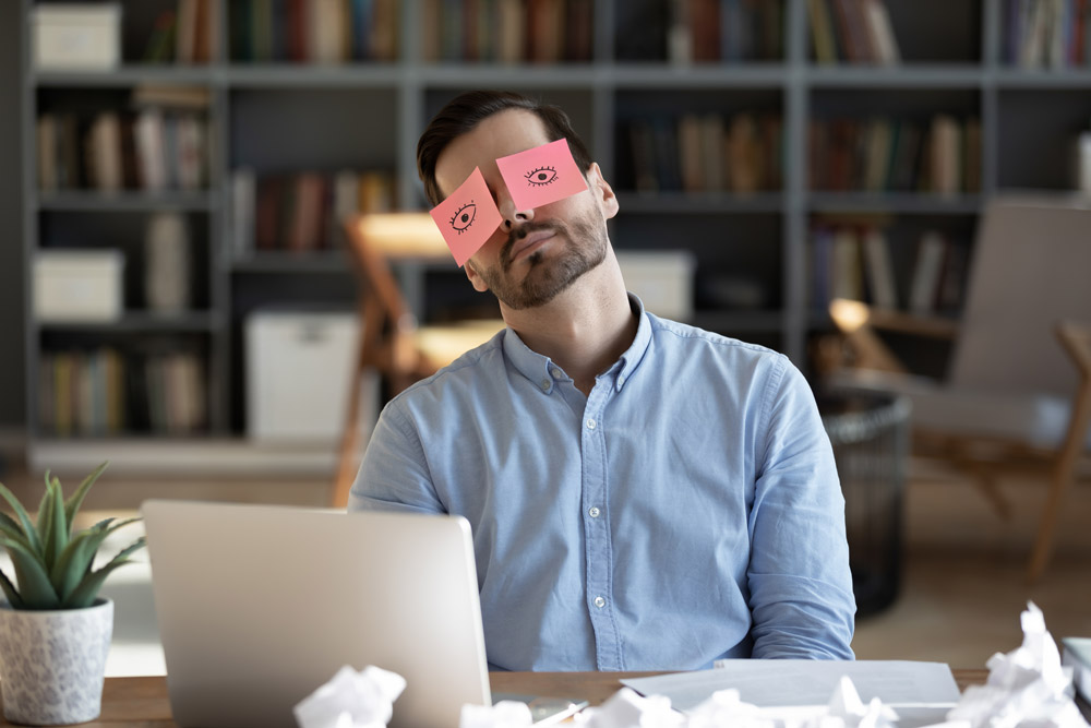 Man taking nap at desk with post-its over eyes.